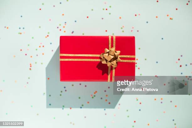 red gift box with glittering gold bow on pastel light blue background with many star shaped confetti. flat lay style - confetti light blue background stock pictures, royalty-free photos & images