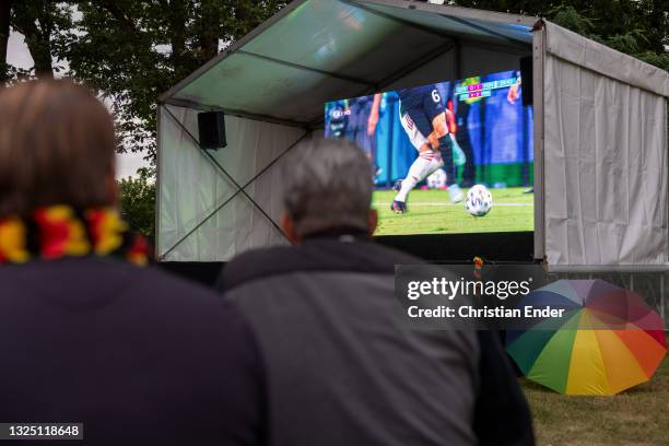 Fans reacting outside in a beer garden while an umbrella in LGBT rainbow colors stands next to the screen on June 23, 2021 in Berlin, Germany....