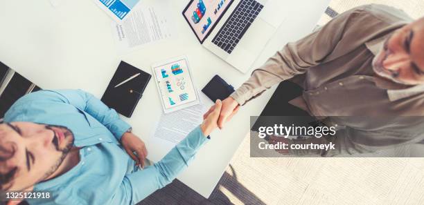 high angle view two businessmen shaking hands in a boardroom. - secret handshake stock pictures, royalty-free photos & images