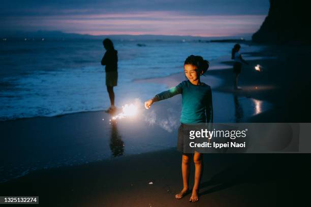 young girl playing with sparkler on beach at dusk - praia noite imagens e fotografias de stock