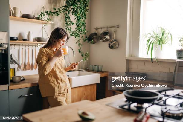 beautiful mature woman talking on the phone in living-room, drinking coffee and having breakfast. morning routine concept. attractive senior woman having conversation on cellphone at home. - coffee relax stockfoto's en -beelden