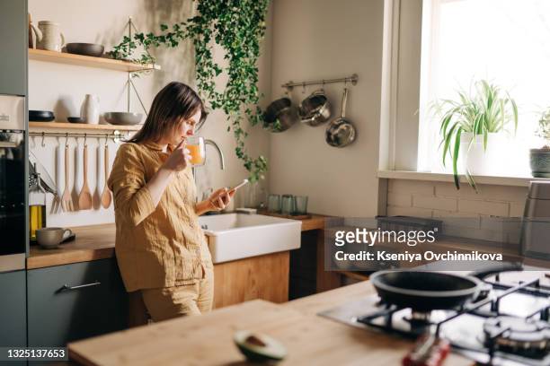 beautiful mature woman talking on the phone in living-room, drinking coffee and having breakfast. morning routine concept. attractive senior woman having conversation on cellphone at home. - person on phone at home bildbanksfoton och bilder