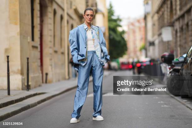Maeva Giani Marshall wears long earrings, a shirt with printed patterns, a white t-shirt, a blue oversized silky / lustrous blazer jacket, matching...