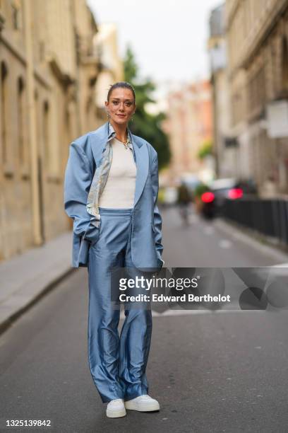 Maeva Giani Marshall wears long earrings, a shirt with printed patterns, a white t-shirt, a blue oversized silky / lustrous blazer jacket, matching...