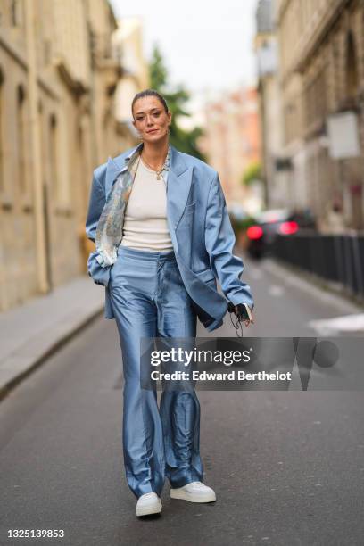 Maeva Giani Marshall wears long earrings, a shirt with printed patterns, a white t-shirt, a blue oversized silky / lustrous blazer jacket, matching...