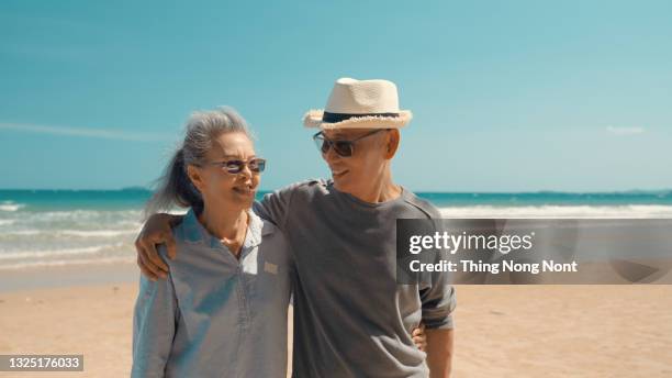 romantic senior couple walking on beautiful tropical beach. mature affectionate couple walking down sandy beach with sea behind and blue sky above - asian senior couple stock pictures, royalty-free photos & images