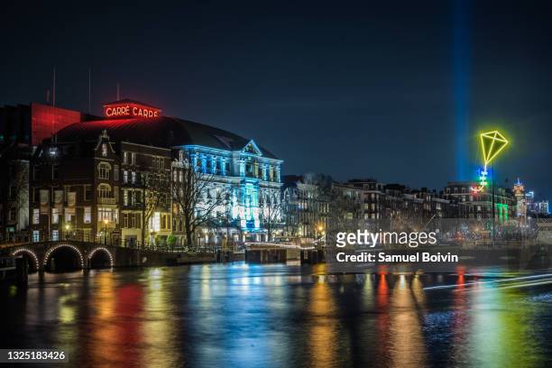 the famous royal theater carré of amsterdam seen at night in long exposure photography from the other bank of the amstel during the amsterdam light festival - fluss amstel stock-fotos und bilder