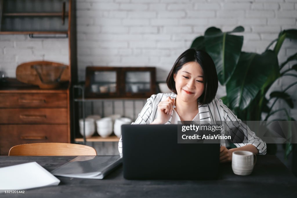 Young Asian woman having online business meeting, video conferencing on laptop with her business partners, working from home in the living room