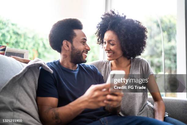 happy couple using smartphone together at home - happy couple using cellphone stockfoto's en -beelden