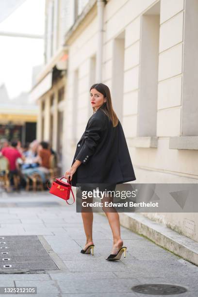 Alexandra Pereira wears gold earrings, an oversized long black blazer jacket from The Frankie Shop, a gold chain belt from Chanel, black ripped denim...