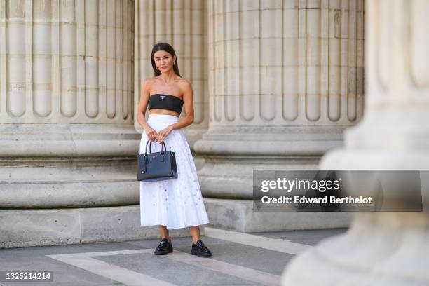 Alexandra Pereira wears silver and gold earrings, a black Prada shoulder-off crop-top, a white high accordion / gathered / pleated midi skirt with...