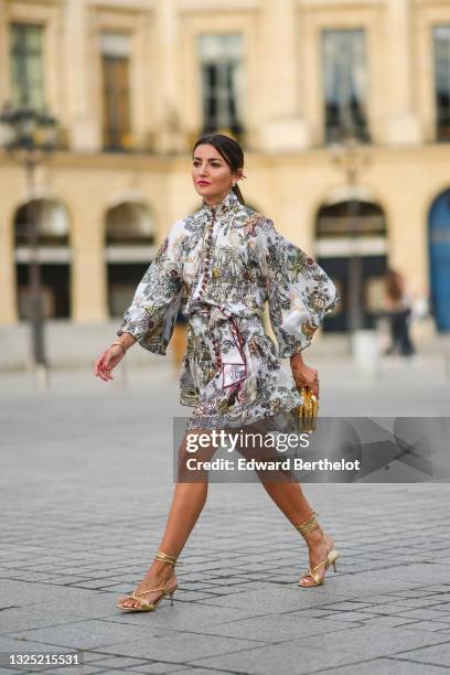 Alexandra Pereira wears gold and pearl earrings, a white with burgundy and pale colors print pattern belted turtleneck dress from Zimmerman with...