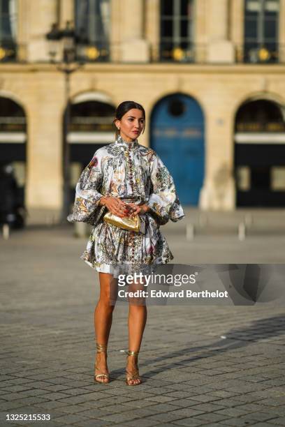Alexandra Pereira wears gold and pearl earrings, a white with burgundy and pale colors print pattern belted turtleneck dress from Zimmerman with...