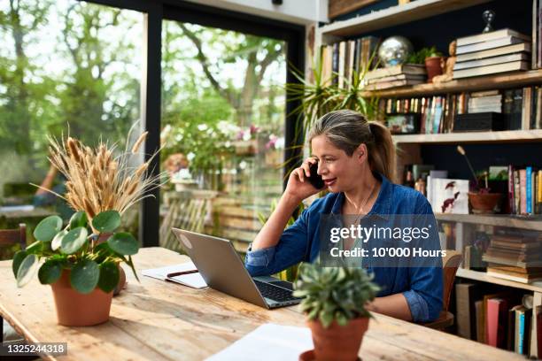 businesswoman using mobile phone in front of laptop - anrufen stock-fotos und bilder