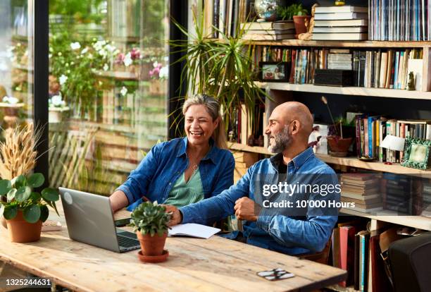 mature couple working from home, talking and laughing - mixed race person stock photos et images de collection