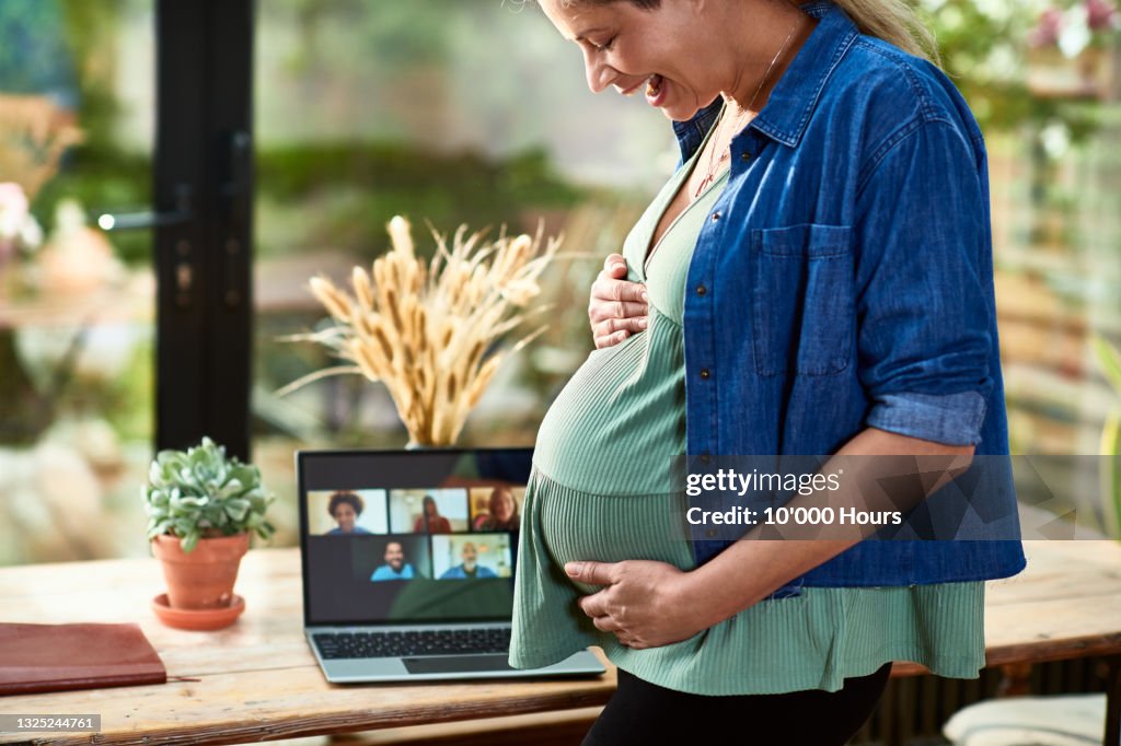 Laughing pregnant woman holding bump on virtual baby shower