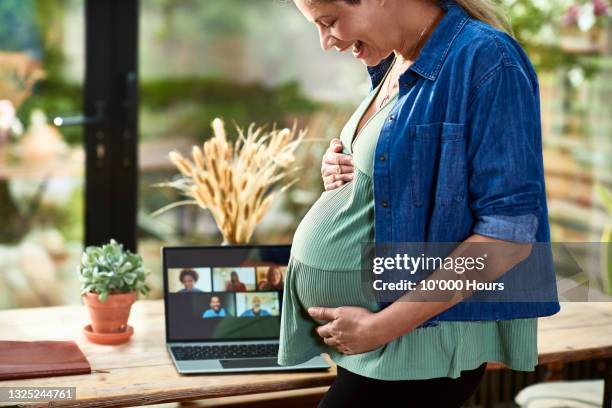 laughing pregnant woman holding bump on virtual baby shower - pregnant belly stockfoto's en -beelden
