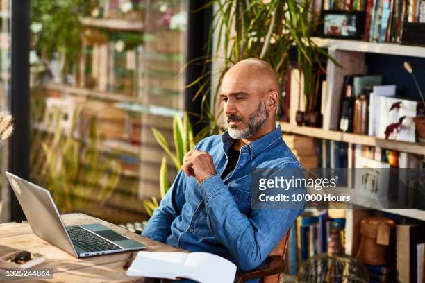 mature businessman sitting at home watching laptop - bald man stockfoto's en -beelden