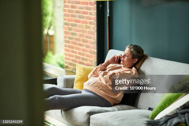 mature pregnant woman sitting on sofa talking on mobile phone - mature asian woman candid foto e immagini stock