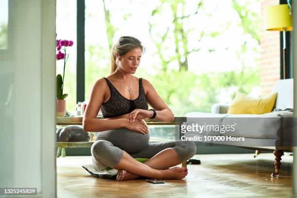 pregnant woman sitting cross-legged on floor checking fitness watch - tummy time stock pictures, royalty-free photos & images