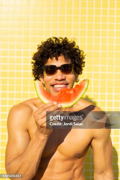man eating a watermelon against a yellow background - muscle men at beach stockfoto's en -beelden
