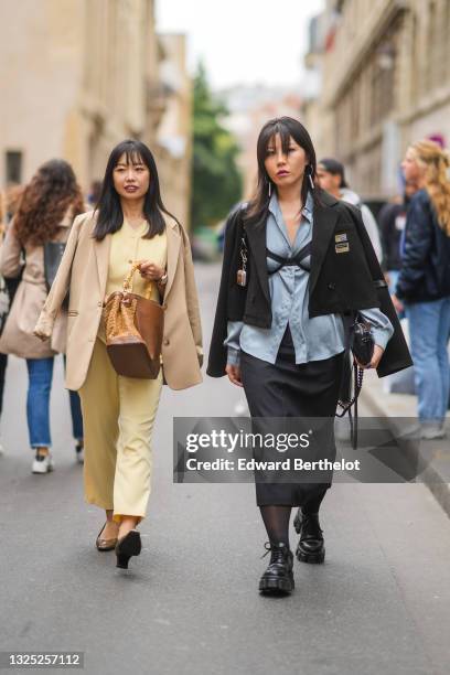 Guest wears a beige long blazer jacket, a pale yellow jumpsuit, a brown shiny leather with a beige wicker part and bamboo handles handbag, a brown...