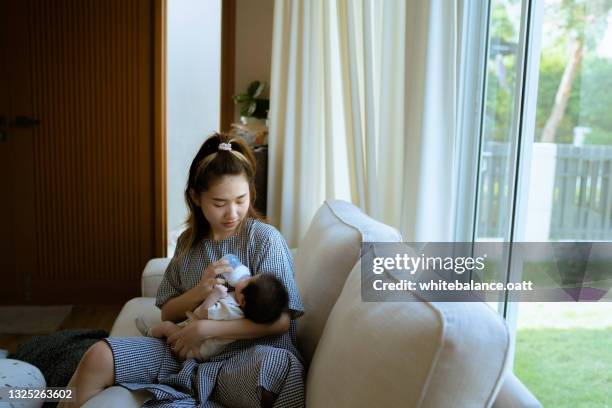 young mother giving milk to her little newborn baby in her arms. - birthing chair stock pictures, royalty-free photos & images