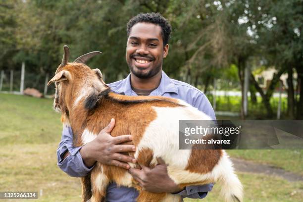 retrato de um jovem trabalhador rural segurando uma cabra - criador de animais - fotografias e filmes do acervo