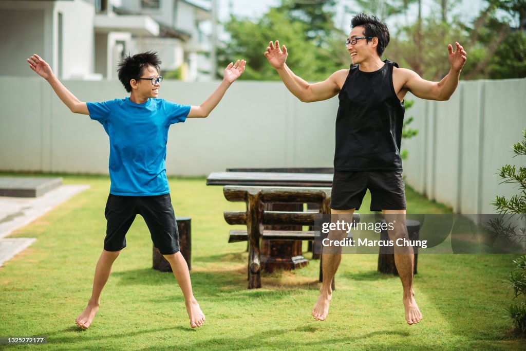 Asian chinese father doing jumping jack together with his son in front yard of house