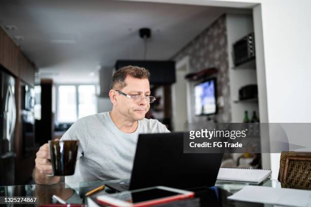 mature man using laptop working at home and drinking coffee - generation x stock pictures, royalty-free photos & images