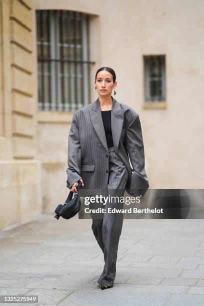 Alexandra Guerain wears silver and black Prada earrings, a black ribbed t-shirt, a gray striped oversized blazer jacket, gray striped matching large...