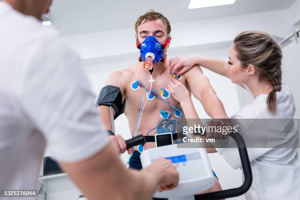 doctors adjusting electrodes during biometric testing on an exercise bike - breath test stockfoto's en -beelden