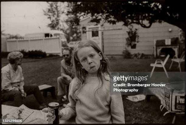 Portrait of a young girl, a can of Mug-brand root beer in her hand, as she makes a face in her backyard, Bellingham, Washington, 1986. Behind her,...