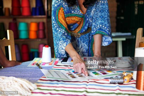 woman wearing a caftan pointing at a color card on a table of textiles - modeontwerper stockfoto's en -beelden
