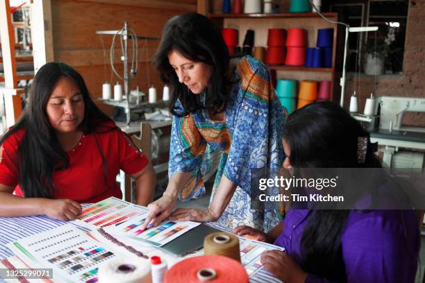 three women working together, one pointing at a color card on a table of textiles - color intensity stock-fotos und bilder