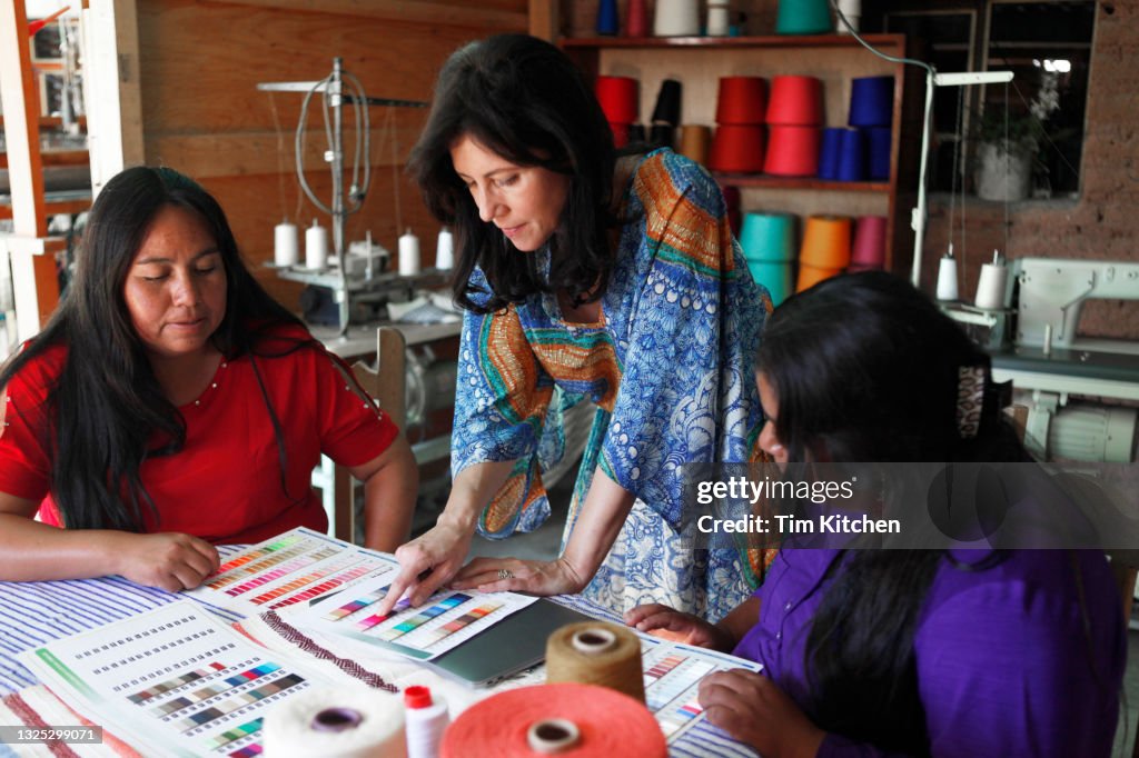 Three women working together, one pointing at a color card on a table of textiles