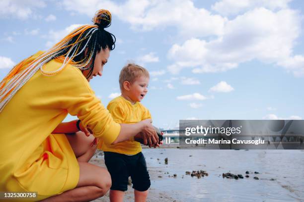 mother with braided hair in yellow outfit with her little son walking in the city park by the sea. - krestovsky stadium view stock pictures, royalty-free photos & images