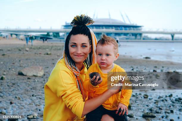 mother with braided hair in yellow outfit with her little son walking in the city park by the sea. - krestovsky stadium view stock pictures, royalty-free photos & images