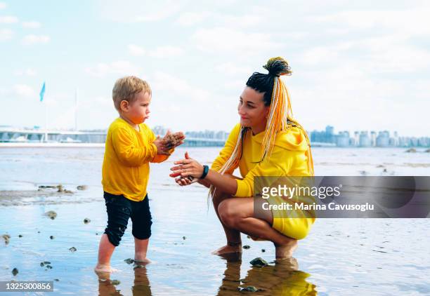 mother with braided hair in yellow outfit with her little son walking in the city park by the sea. - krestovsky stadium view stock pictures, royalty-free photos & images