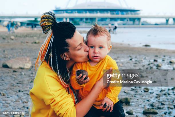 mother with braided hair in yellow outfit with her little son walking in the city park by the sea. - krestovsky stadium view stock pictures, royalty-free photos & images