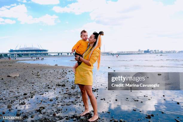 mother with braided hair in yellow outfit with her little son walking in the city park by the sea. - krestovsky stadium view stock pictures, royalty-free photos & images