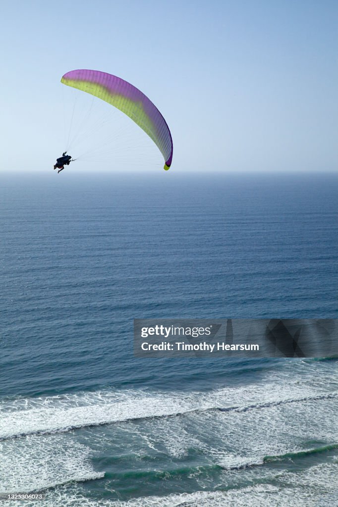 Single paraglider over the ocean as waves roll in