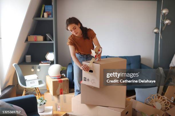 a young woman is packing her moving boxes - desempaquetar fotografías e imágenes de stock