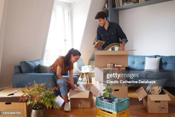 a young couple packing/unwrapping moving boxes - unpacking stock pictures, royalty-free photos & images
