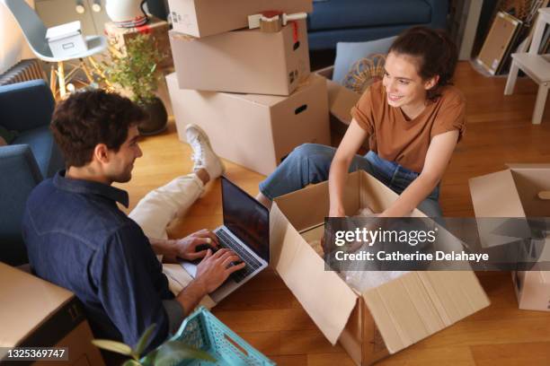 a young couple packing/unwrapping moving boxes - move fotografías e imágenes de stock