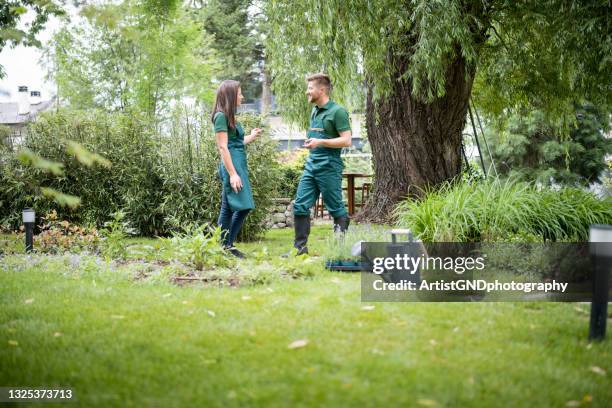 gardeners in uniform standing in beautiful garden and talking about landscaping ideas. - professional landscapers stock pictures, royalty-free photos & images