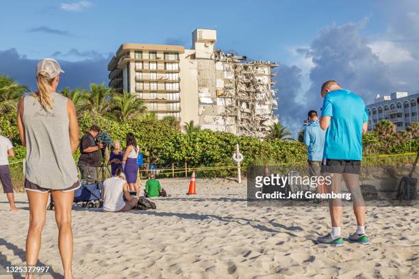 News media crew reporting and local residents on the beach looking at the collapsed Champlain Towers condimium, Surfside, Miami Beach, Florida.