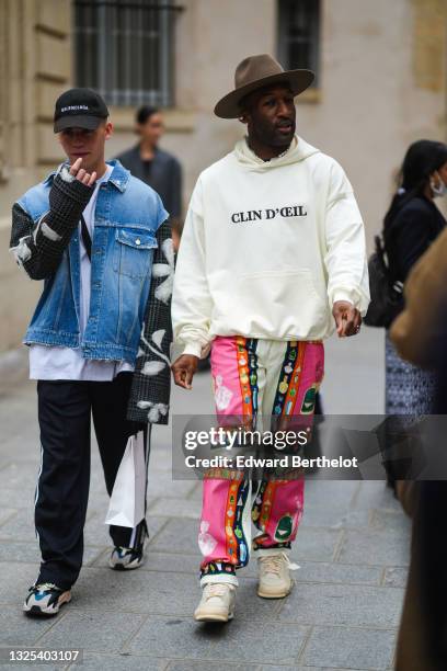 Guest wears a brown felt hat, silver earrings, a half pearls and half chain necklace, a white hoodie sweater with 'Clin D'Oeil" slogan, white neon...