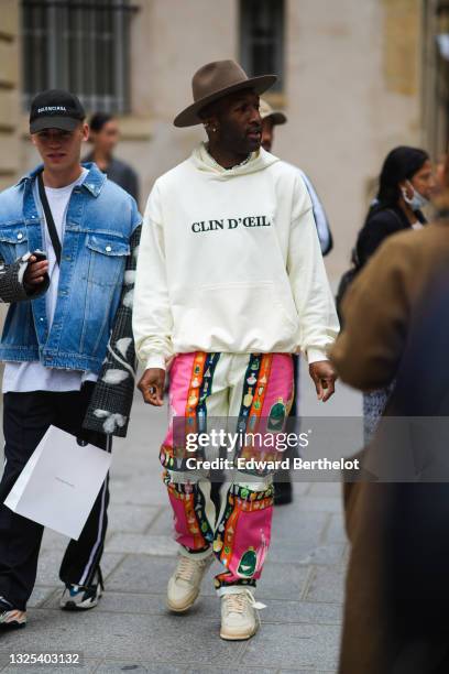 Guest wears a brown felt hat, silver earrings, a half pearls and half chain necklace, a white hoodie sweater with 'Clin D'Oeil" slogan, white neon...