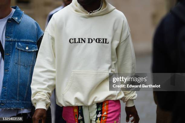 Guest wears a half pearls and half chain necklace, a white hoodie sweater with 'Clin D'Oeil" slogan, white neon pink and orange and navy blue with...